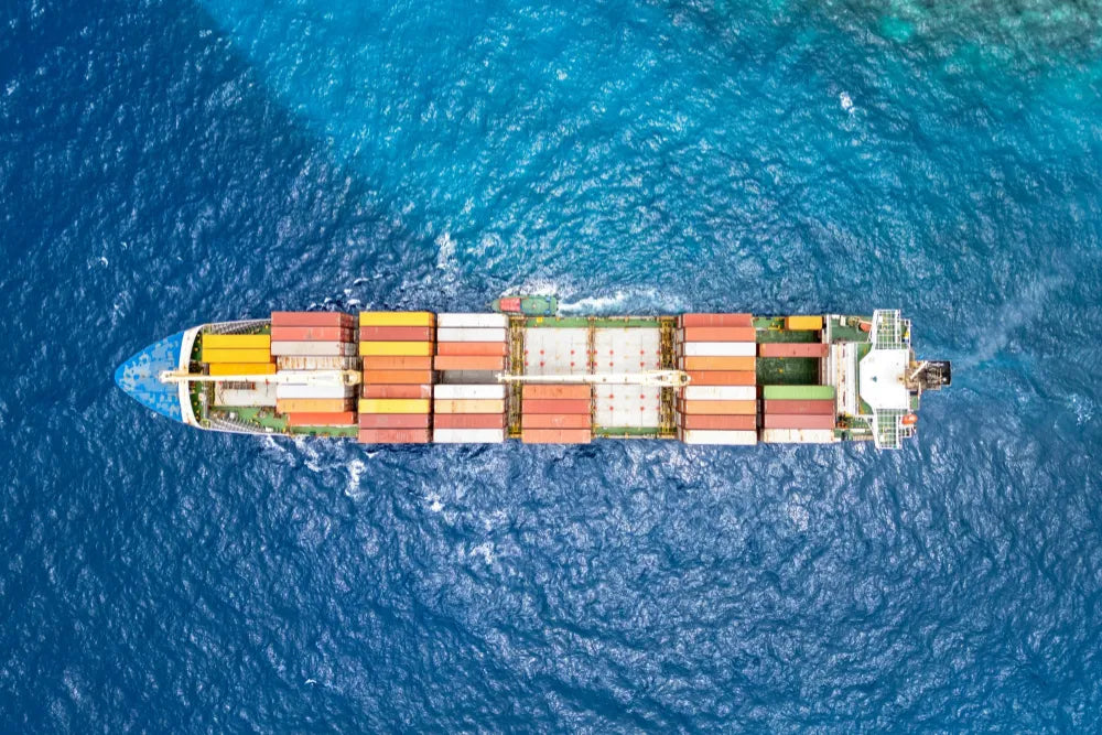 Aerial view of a cargo ship transporting colorful shipping containers across the ocean, representing global freight and international shipping.
